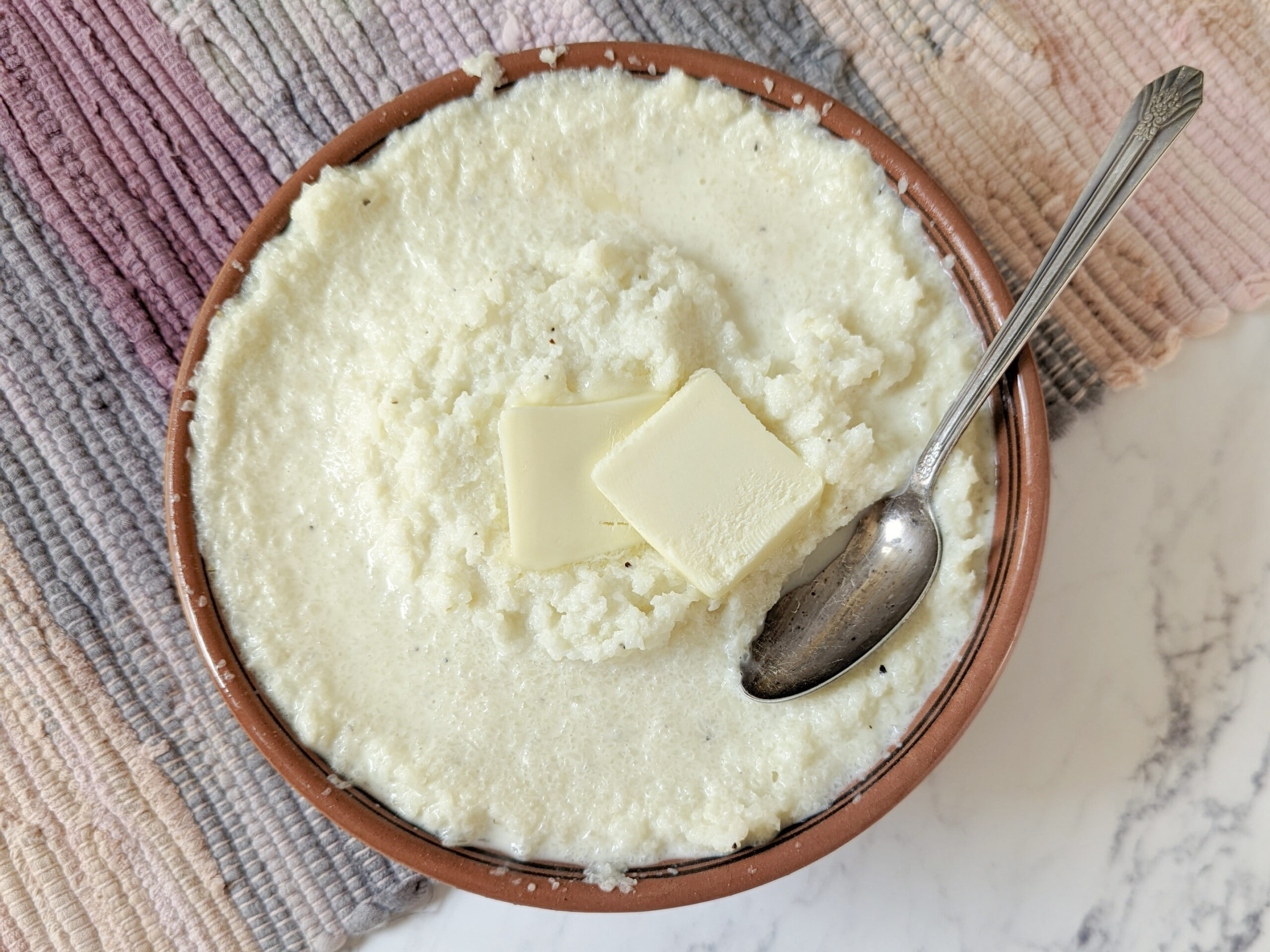 Mashed cauliflower in a serving bowl with a tab of butter.