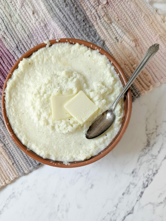 Mashed cauliflower in a serving bowl with a tab of butter.