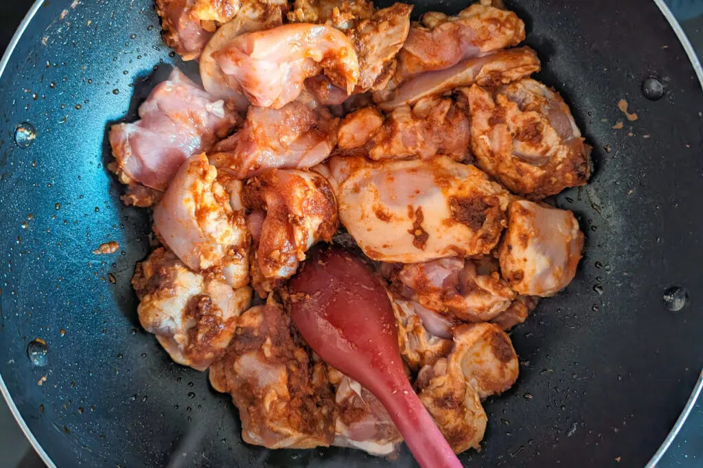 Chicken thighs searing in curry paste.