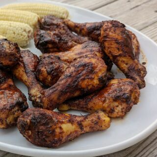 A serving platter of bbq baked chicken legs and corn on the cob ready to be served.