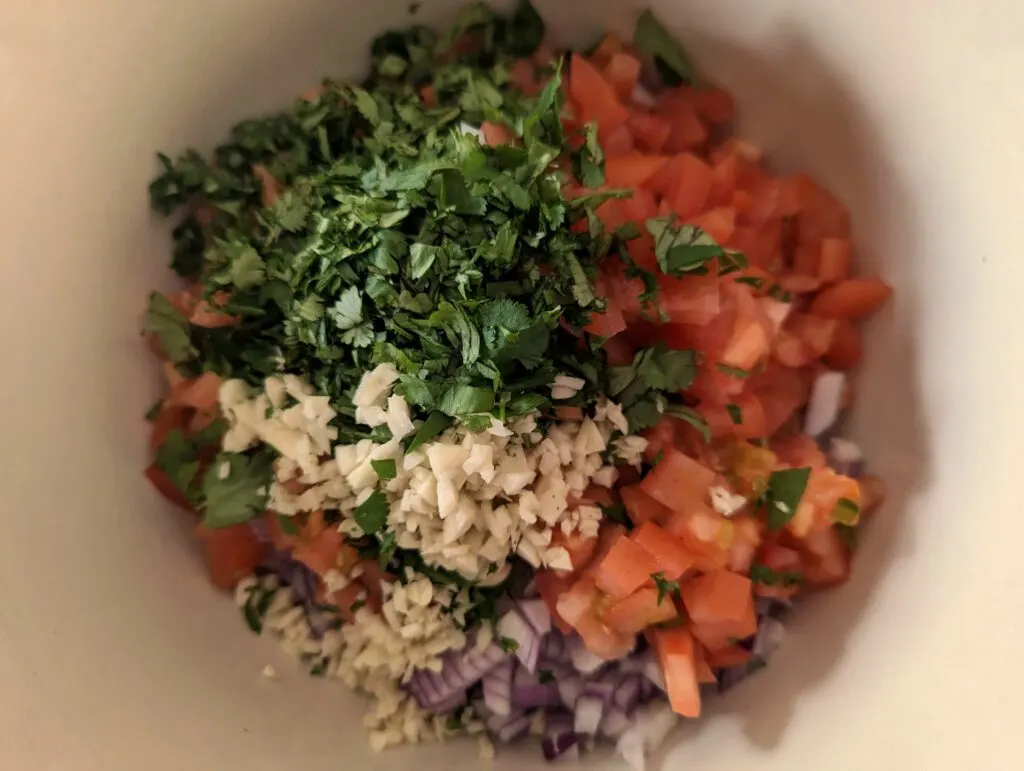 Cilantro, garlic, and onions dded to the tomatoes in a bowl.