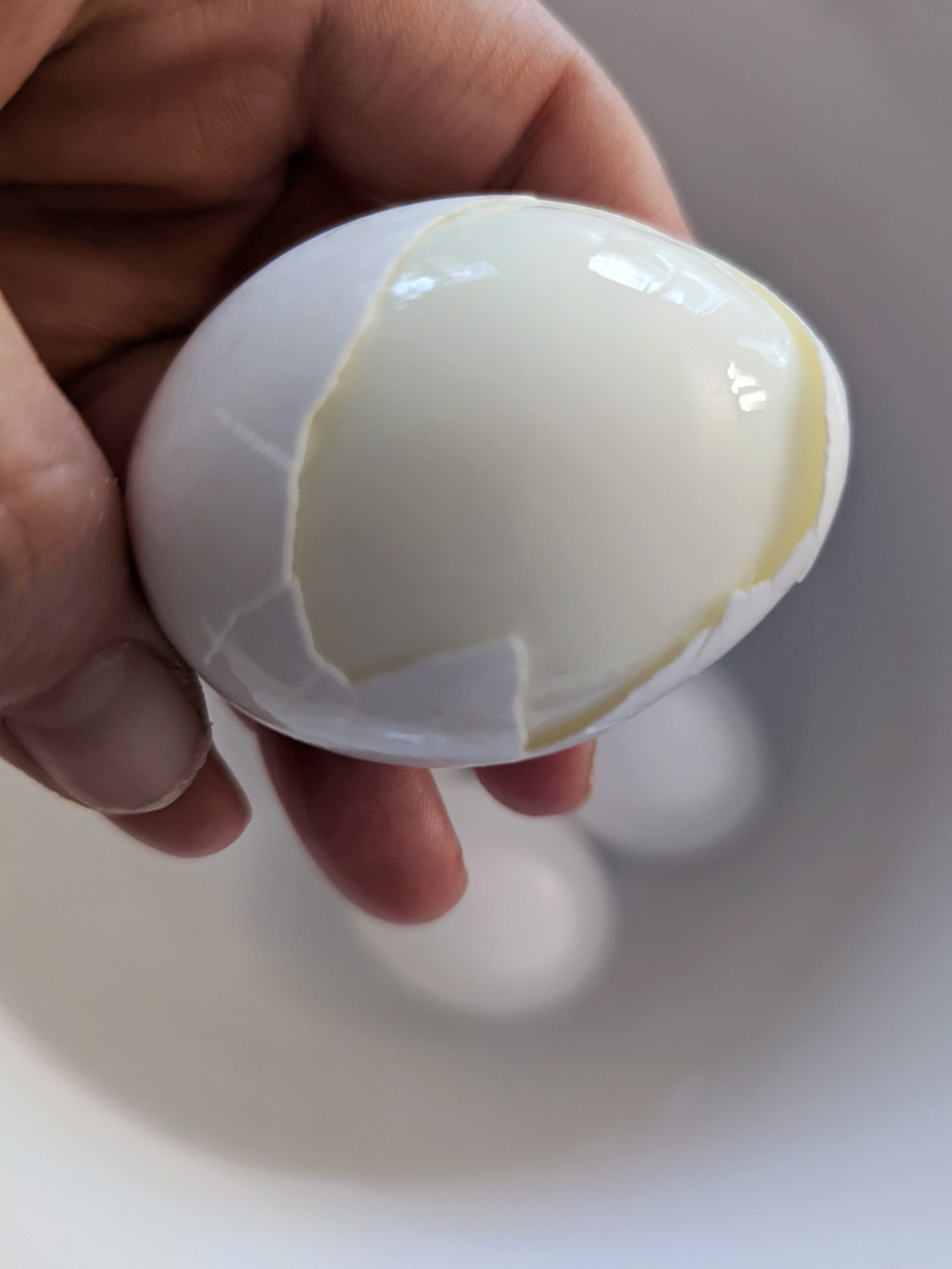A hand holding a cracked hard boiled egg.