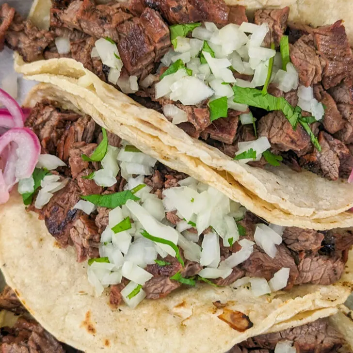 Three carne asada tacos with toppings.