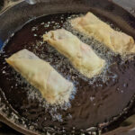 Corned Beef and Cabbage Egg Rolls frying in oil.