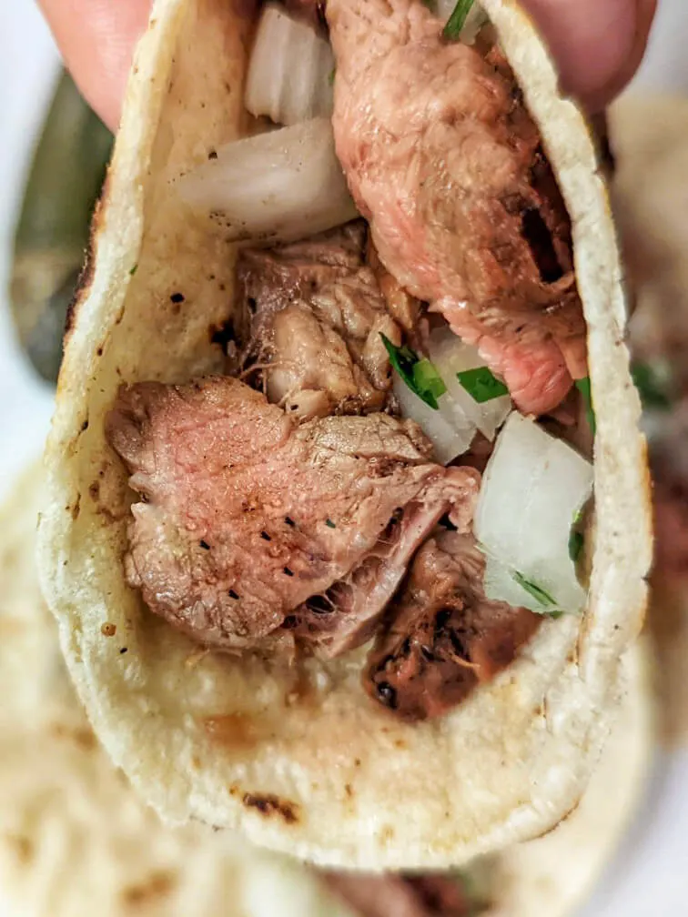 A close up of a carne asada taco topped with cilantro and onion.