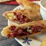 Cut open corned beef and cabbage egg rolls with horseradish cream sauce on a plate.