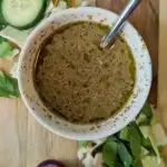 A small bowl of homemade salad dressing with vegetables all around it.