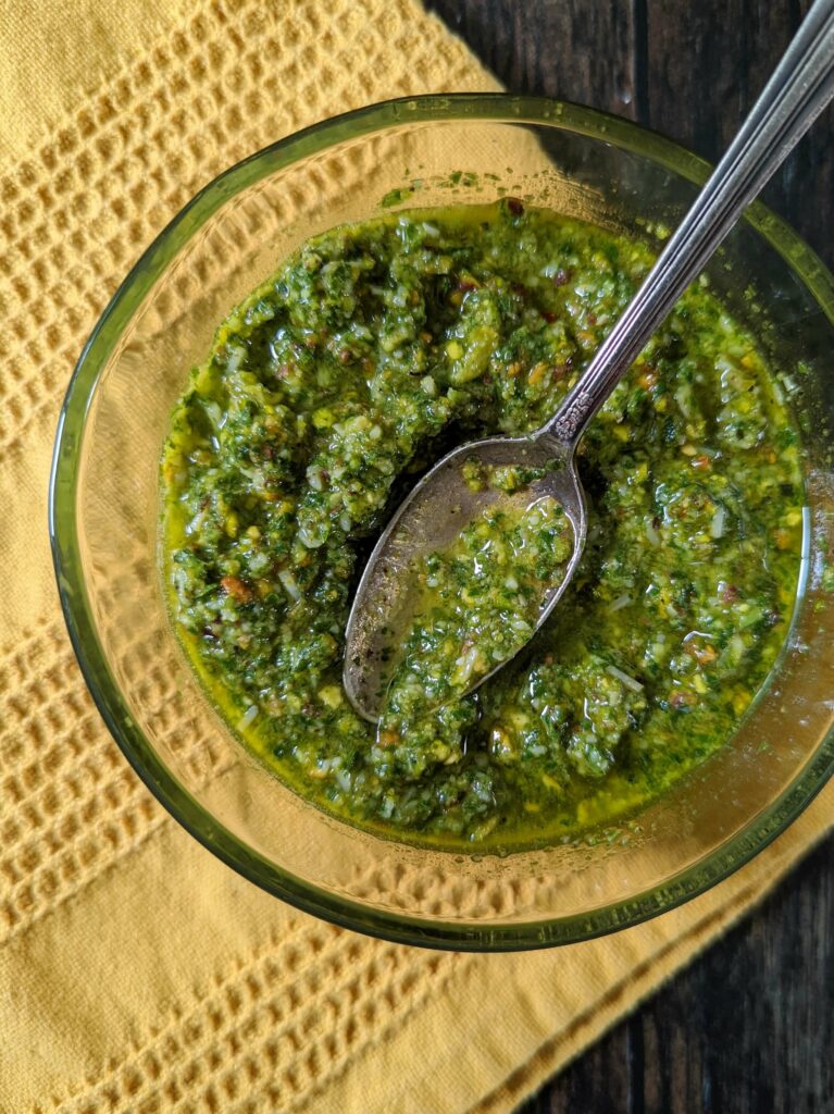 Pesto in a glass bowl with a spoon scooping into it. 
