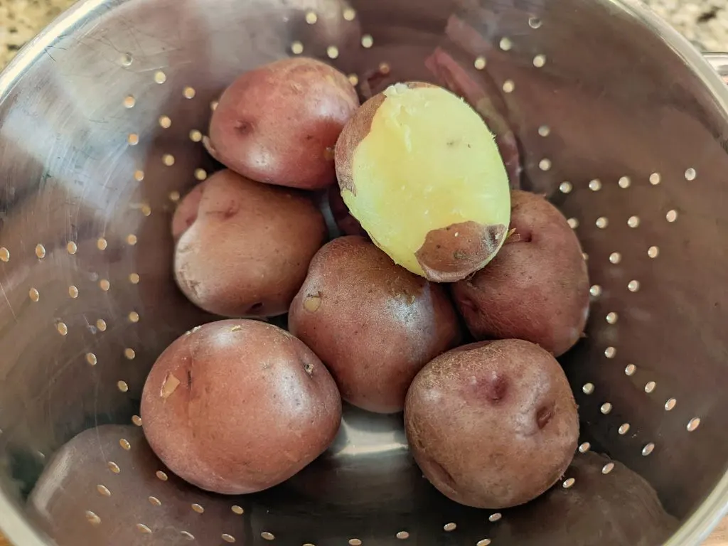 Cooled down potatoes in a colander being peeled. 