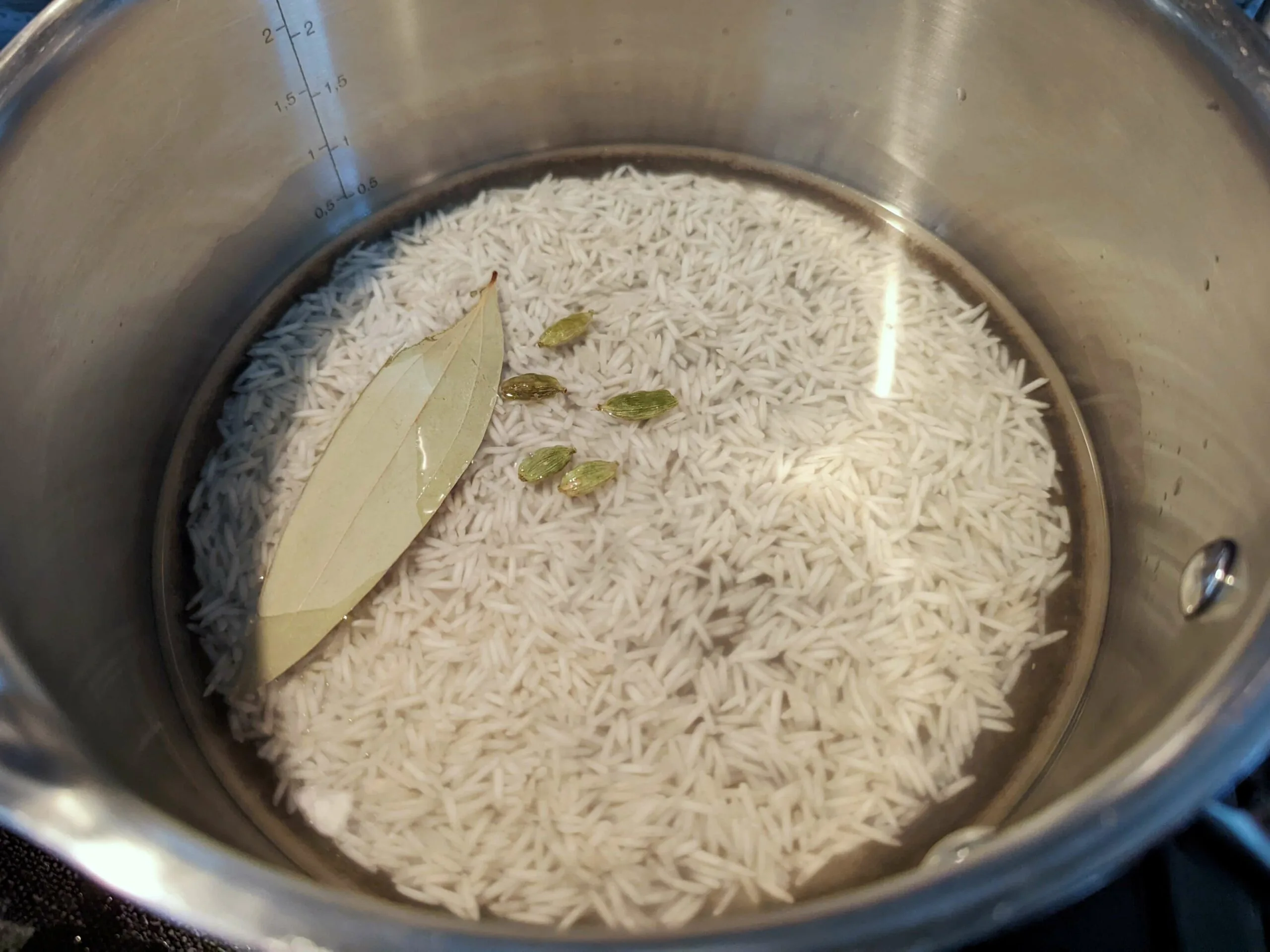 Rice, water, bay leaves, and cardamom added to a sauce pan.
