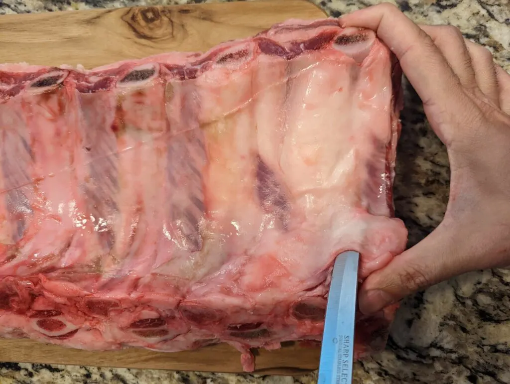 A knife sliding under the membrane of the beef ribs.