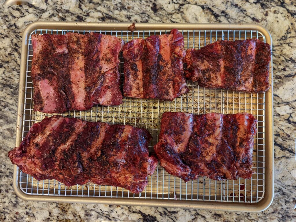 Beef ribs seasoned with rib rub on a baking sheet.