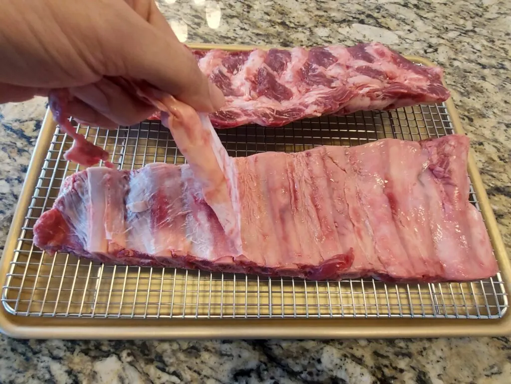 A hand peeling back the membrane from the beef ribs.