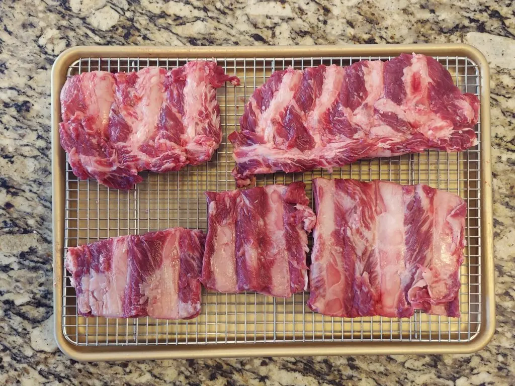 Beef ribs cut into slabs on a rimmed baking sheet.
