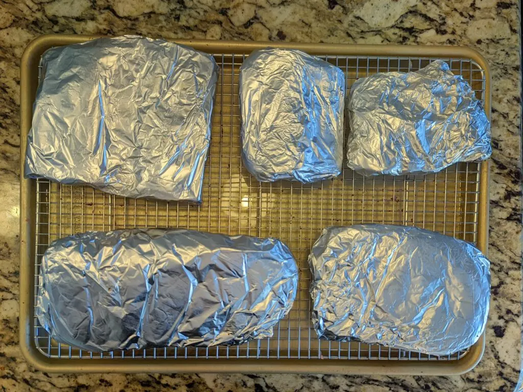 Beef ribs slabs wrapped in foil on a baking sheet.