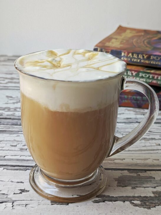 A glass of butterbeer recipe topped with homemade whipped cream with Harry potter books in the background.