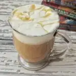 A glass of Harry Potter butterbeer recipe topped with homemade whipped cream and Harry potter books in the background.