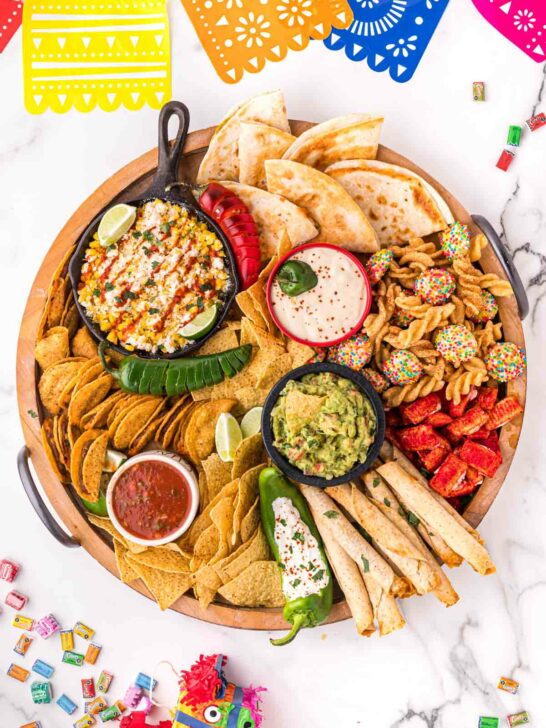 A Mexican charcuterie board with taquitos, tacos, elote, guacamole, and other treats.
