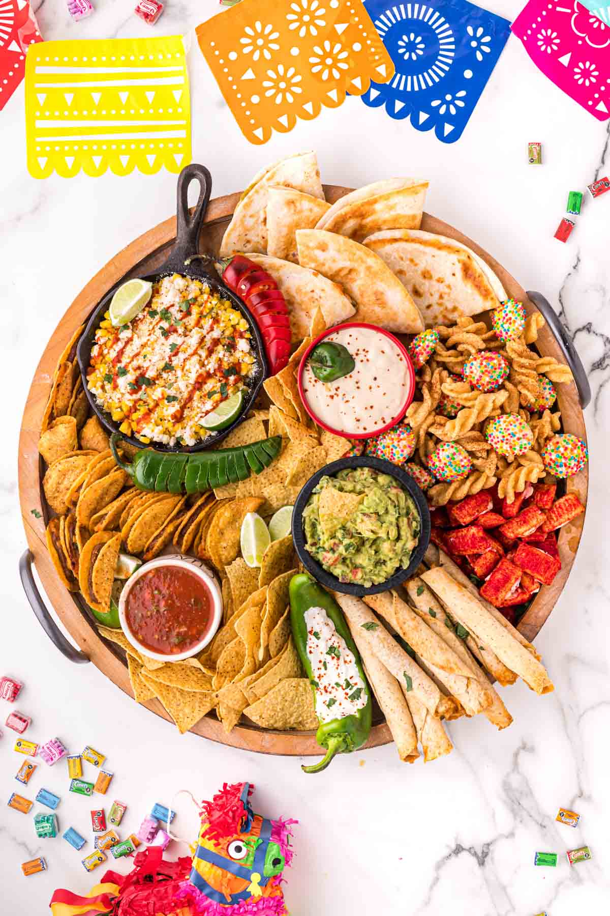 A Mexican charcuterie board with taquitos, tacos, elote, guacamole, and other treats.