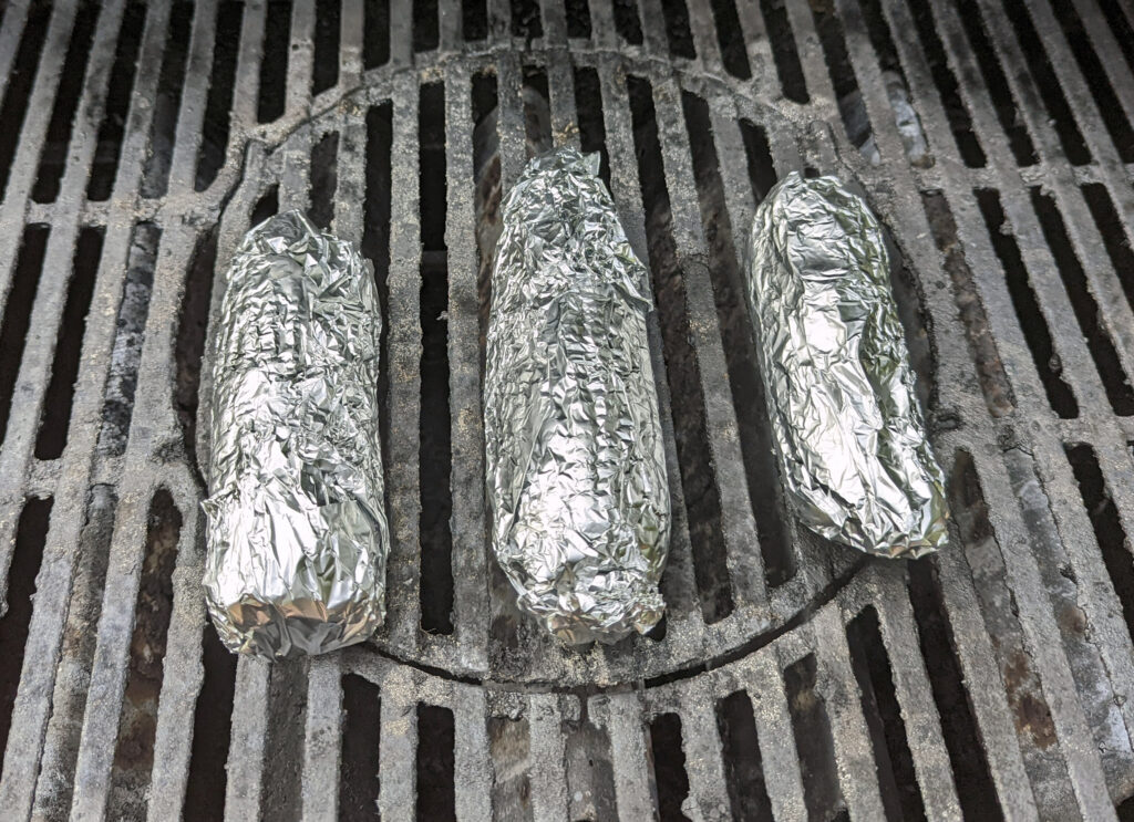 Foil-wrapped corn on the cob cooking on the grill.