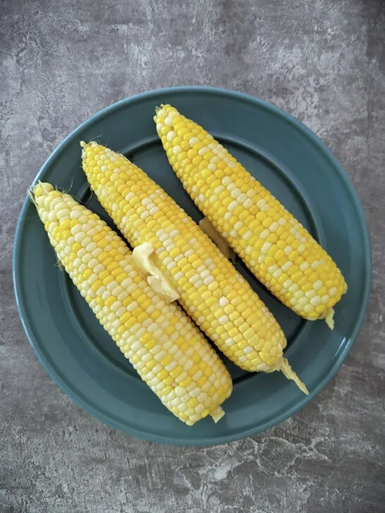 Corn on the cob on a plate coated in butter.
