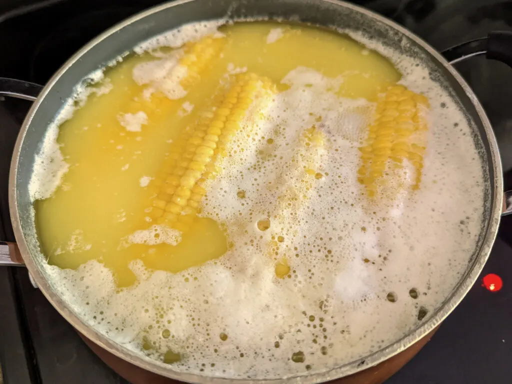 Corn on the cob boiling in a pot with milk and butter.