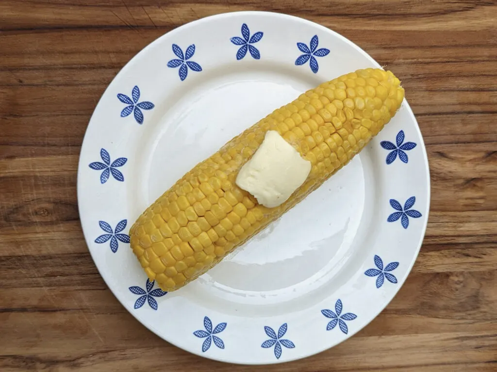 A table of butter on a cooked ear of corn.