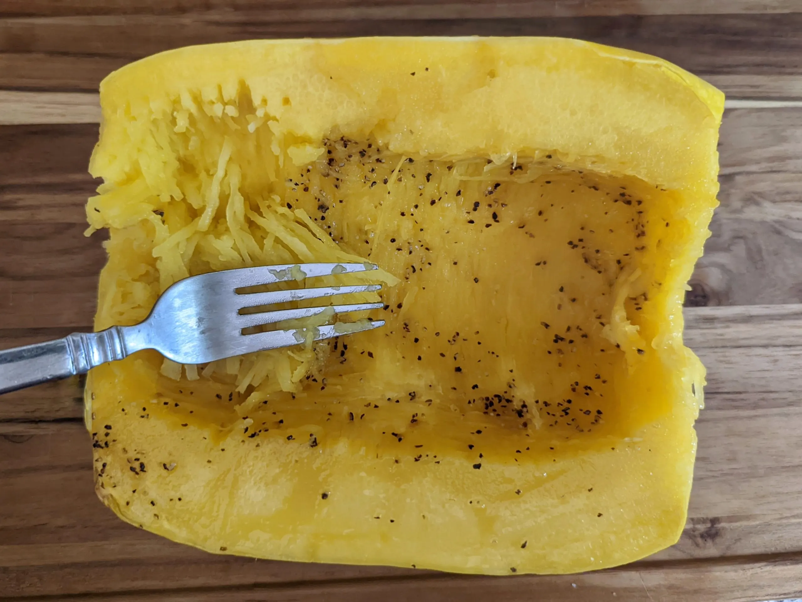 A cooked half of a spaghetti squash being shredded with a fork.