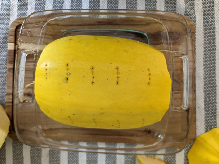 A spaghetti squash half set into a glass dish and poked with a fork.