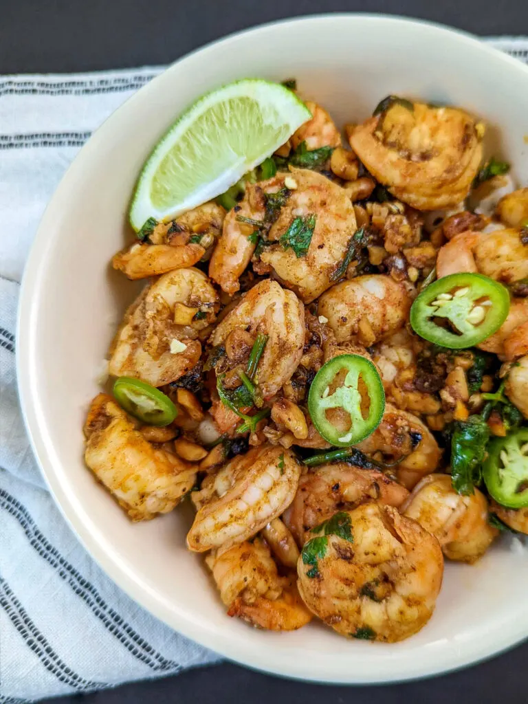 A bowl of pan seared shrimp garnished with cilantro, chilies, and lime wedges. 