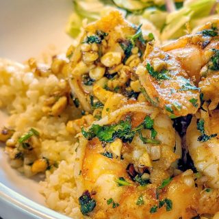There is a serving of pan-seared shrimp over cauliflower rice with a tossed salad in the background.