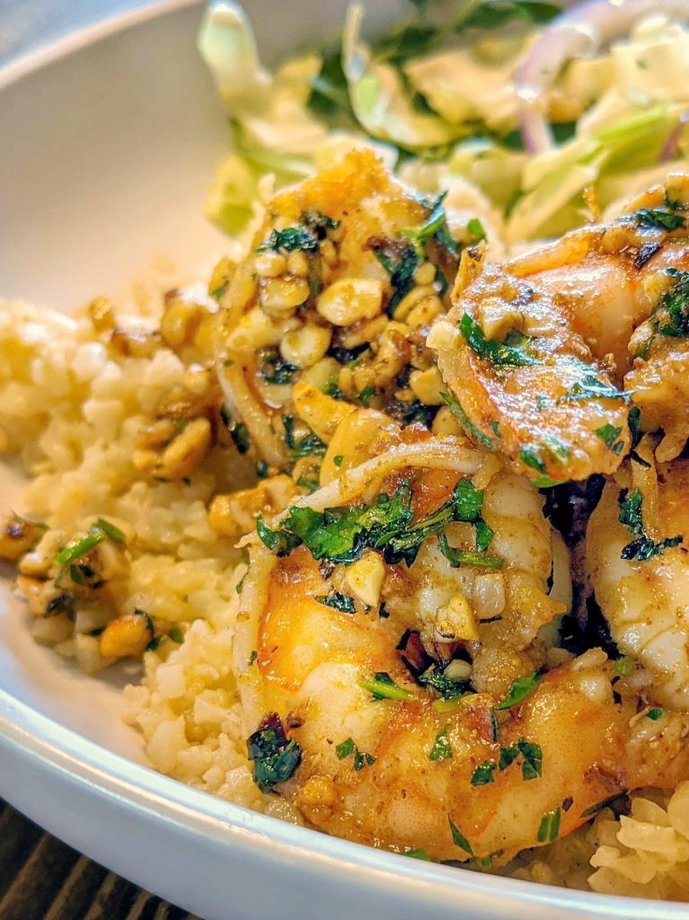 There is a serving of pan-seared shrimp over cauliflower rice with a tossed salad in the background.