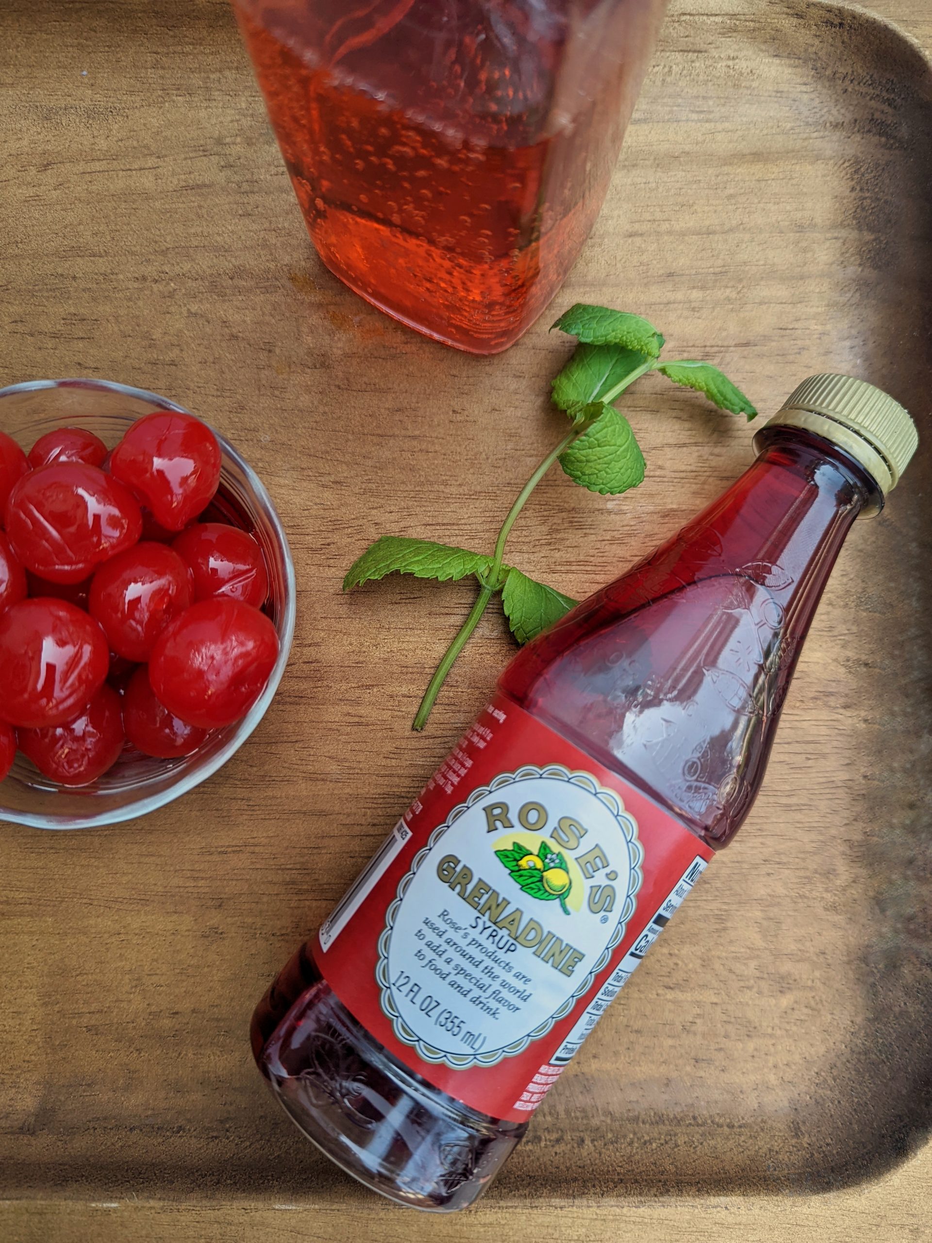 A bottle of grenadine next to mint and cherries.