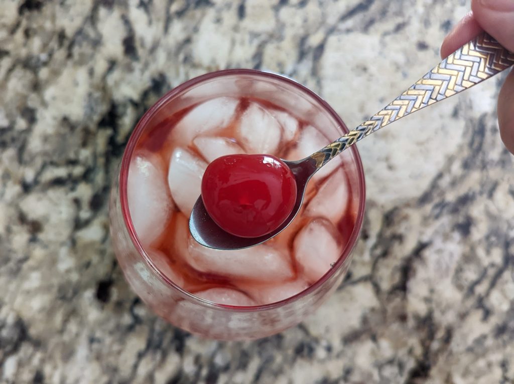A cherry held over the shirley temple drink.