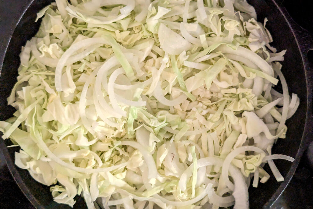 Cabbage and onions sautéing in a skillet.