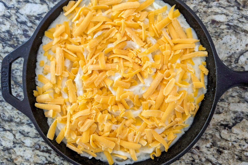 A skillet of rumbledethumps topped with shredded cheese.