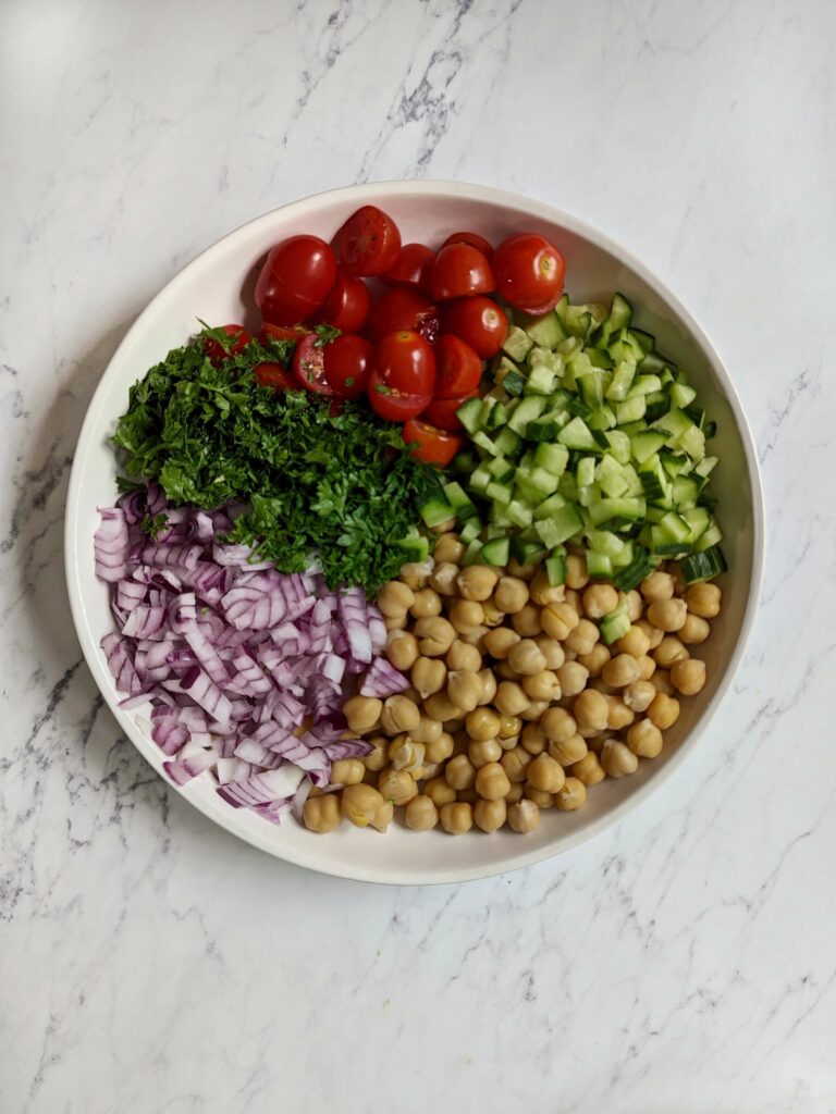 Add the vegetables for chickpea salad on a plate.