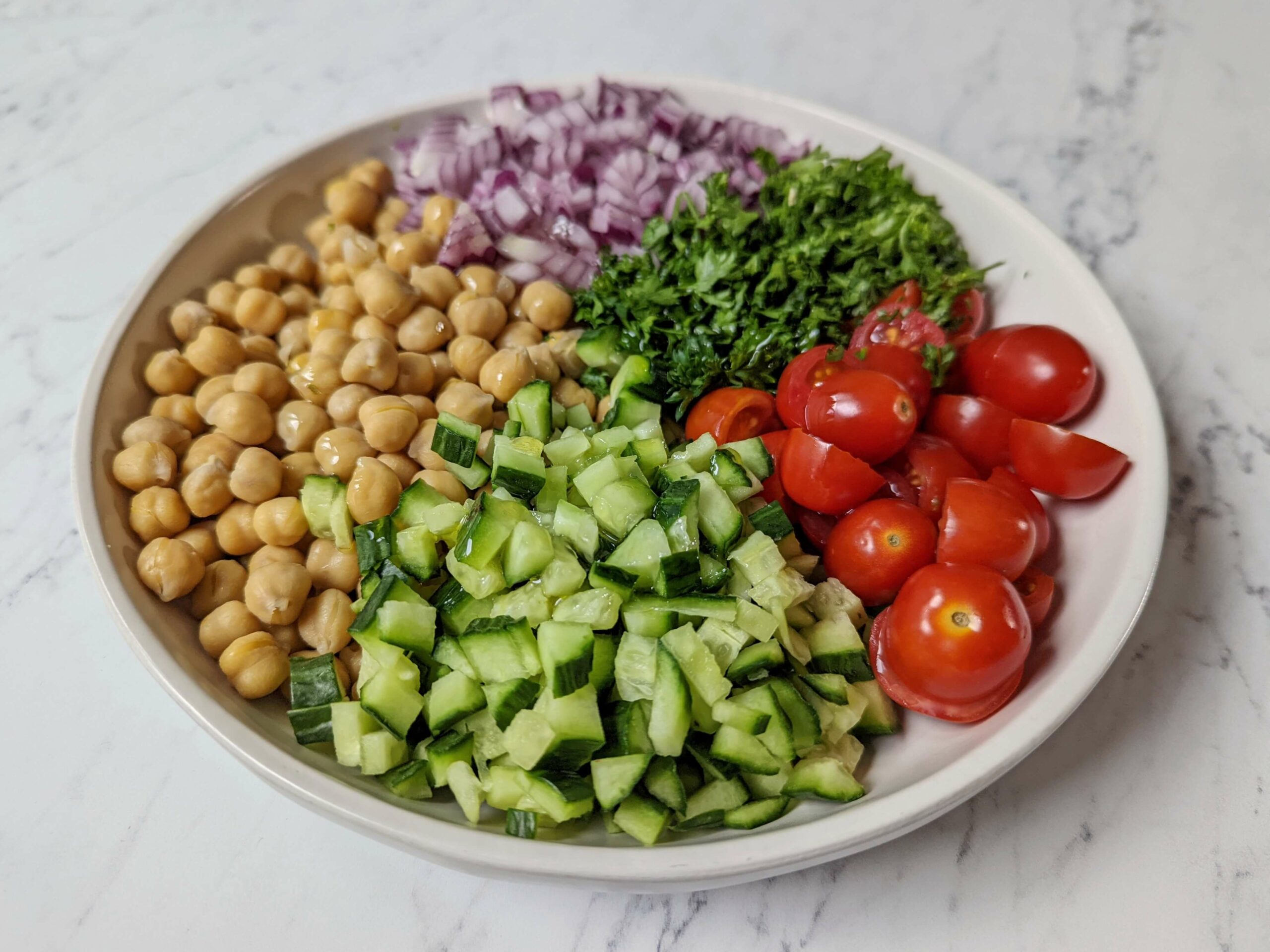 Add the vegetables for chickpea salad on a plate.