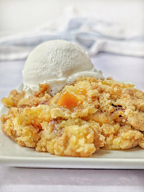 Easy peach cobbler with cake mix on a plate topped with whipped cream.