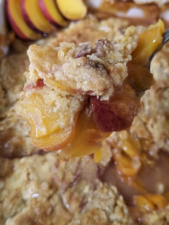 A scoop of peach cobbler over the baking dish of easy peach cobbler with cake mix.
