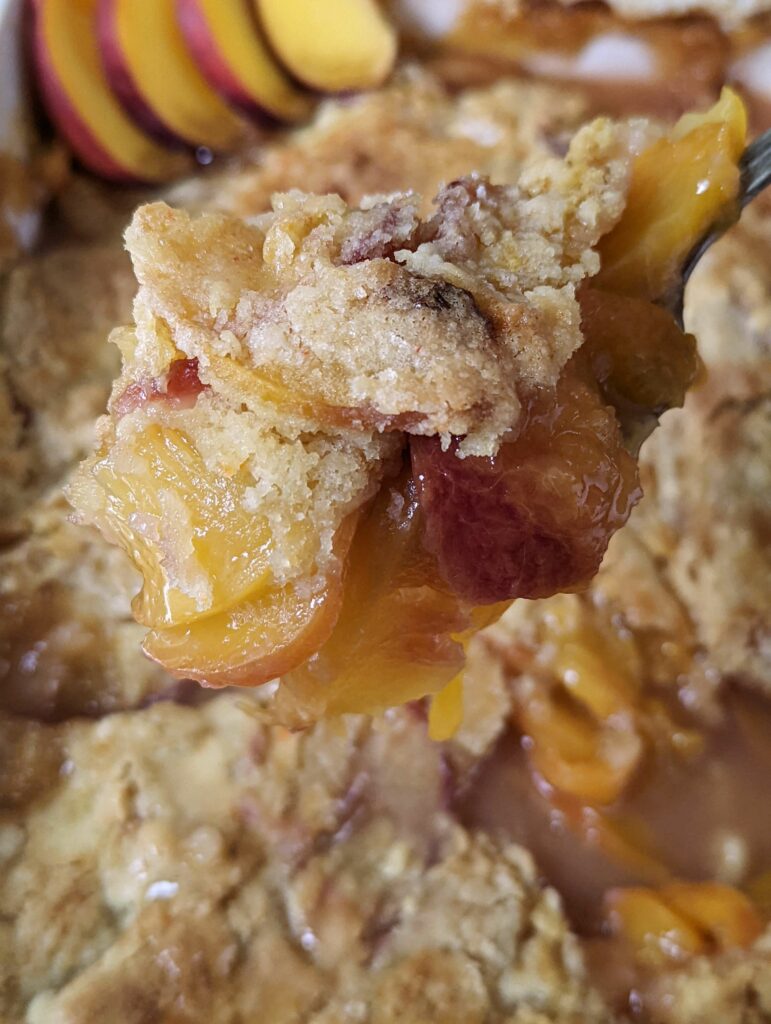 A scoop of peach cobbler over the baking dish of cobbler.