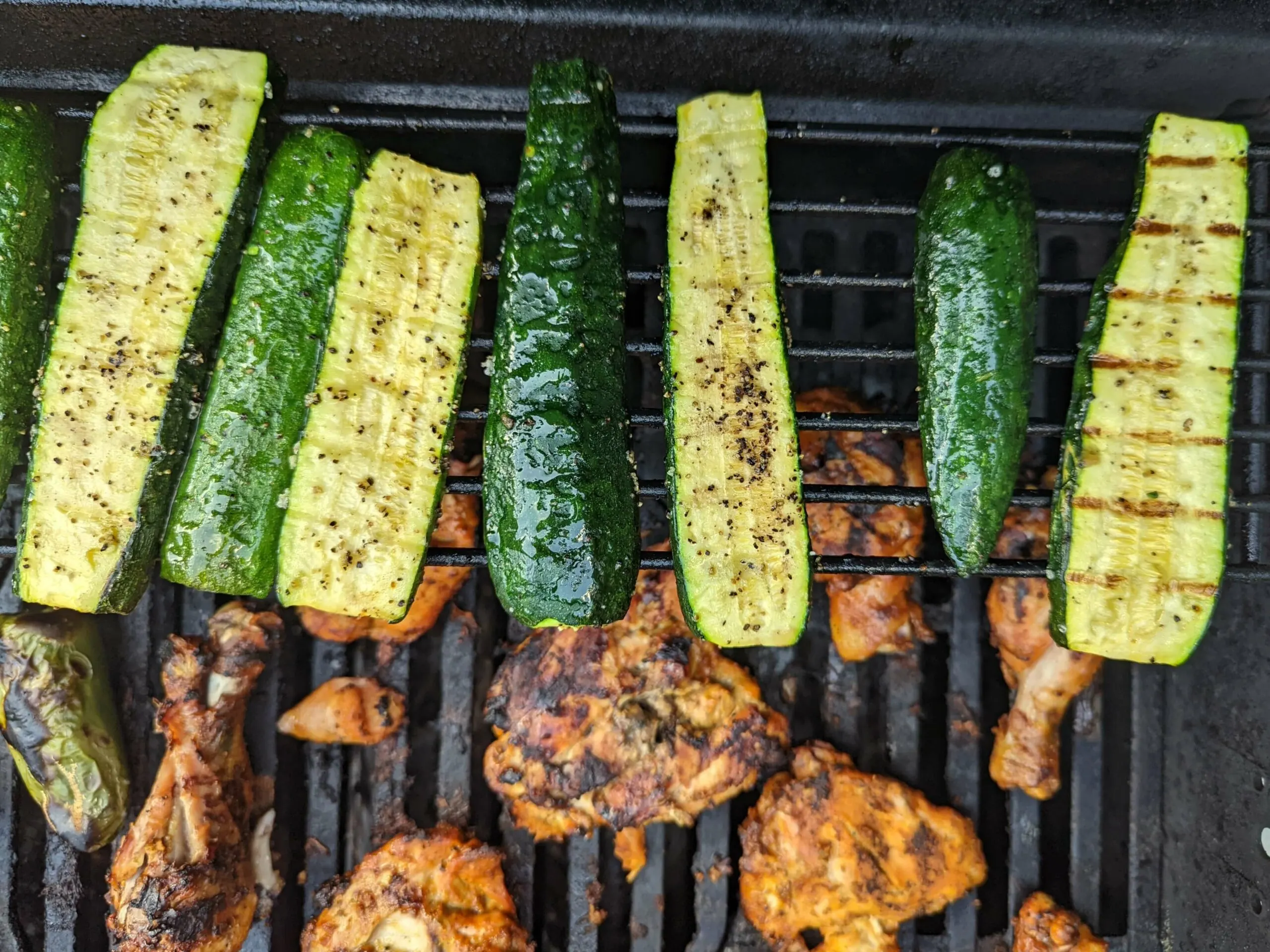 Zucchini cooking on the grill with chicken grilling in the background.