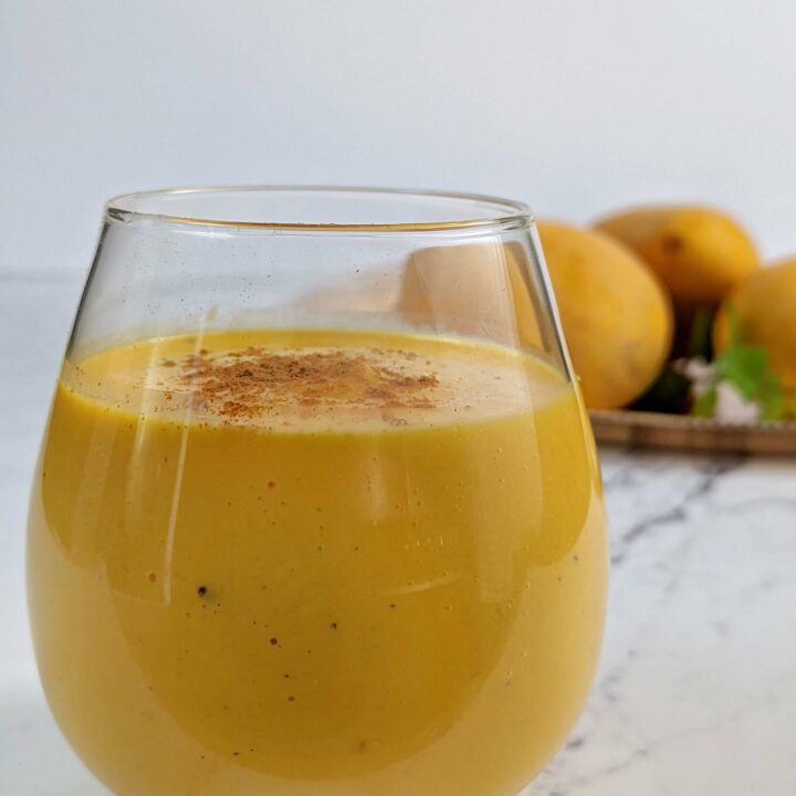 Mango lassi in a mug with mangos in the background.