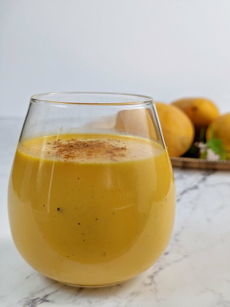 Mango lassi in a mug with mangos in the background.