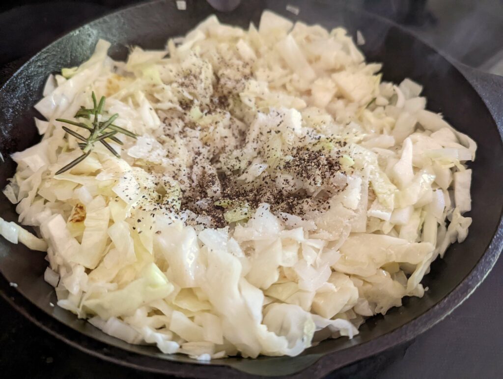 Seasoning added to onions and cabbage cooking in a skillet.