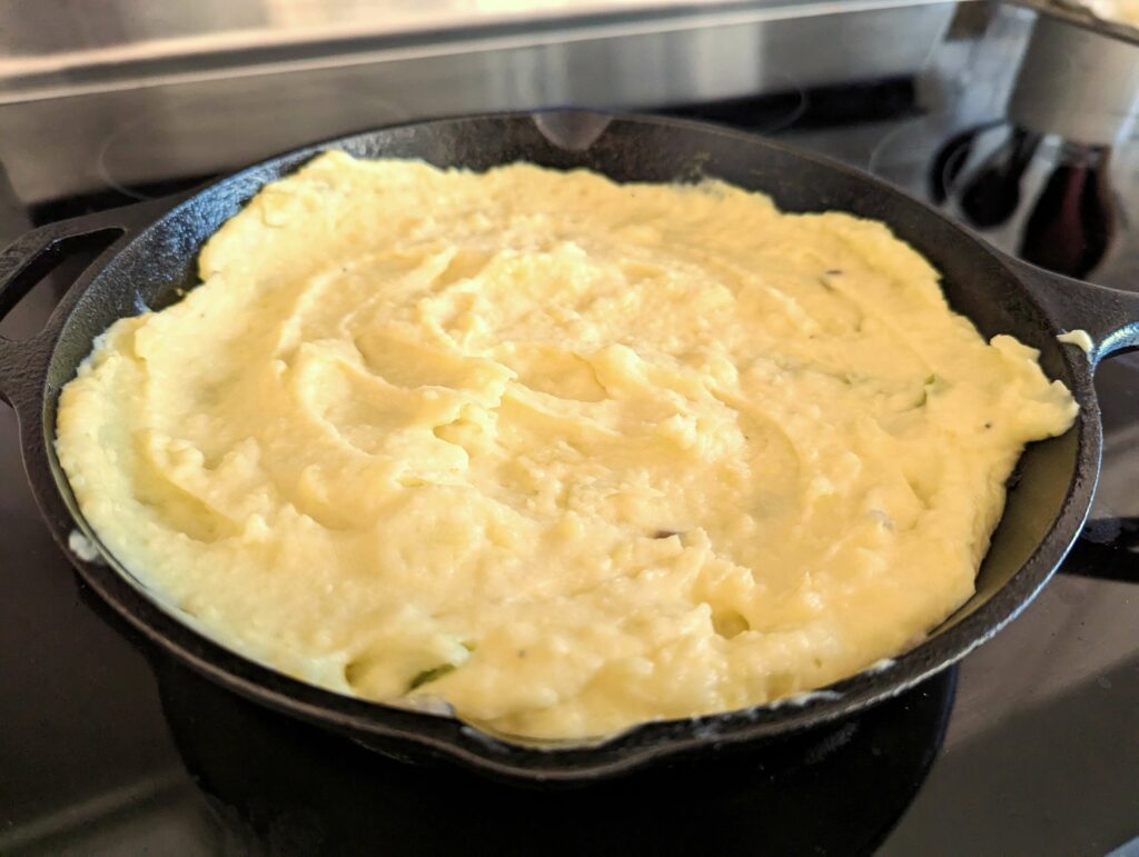 A skillet of vegetables topped with mashed potatoes.