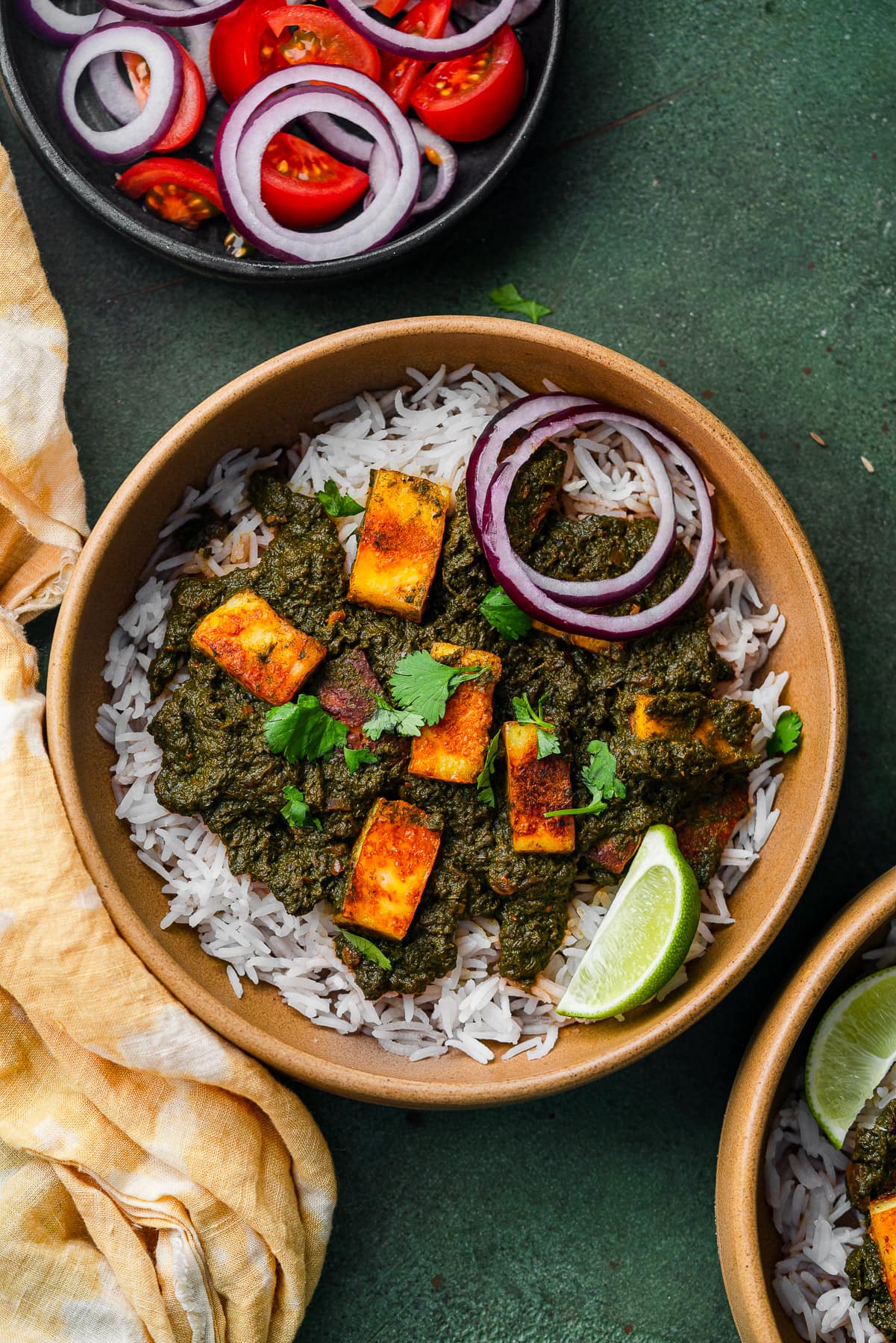 Saag paneer served over rice and garnished with fresh onion and lime.