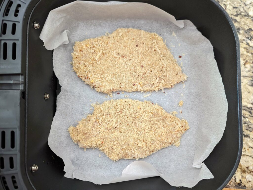 Two breaded chicken breasts cooking in the air fryer.