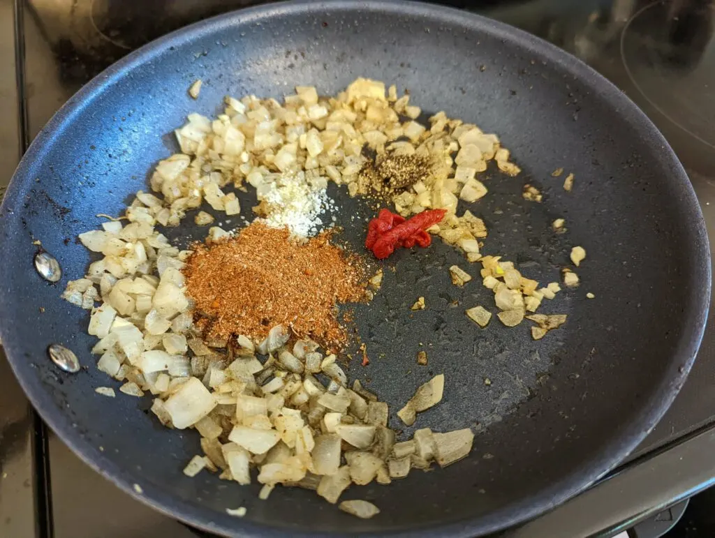 Spices added to the cooking onions in a skillet.