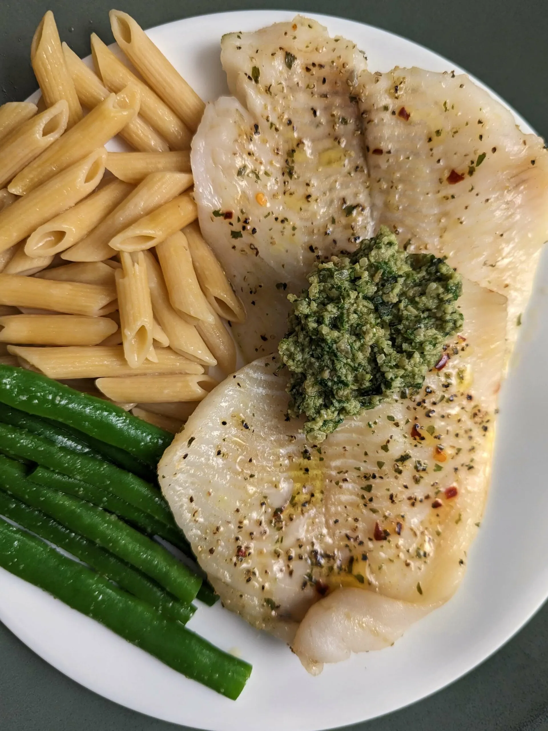 Our baked flounder topped with homemade pesto and served on a plate pasta and green beans.